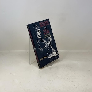 Könnte beinhalten: Ein Hardcover-Buch mit dem Titel "Benjamin Franklin & Polly Baker" von Max Hall. Das Cover zeigt eine Schwarz-Weiß-Illustration einer Person und den Titel in roter und weißer Schrift. Das Buch wird auf einem transparenten Acrylständer präsentiert.