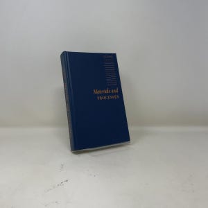 May include: A dark blue hardcover book titled Materials and Processes in gold lettering on the front cover. The cover features a series of thin horizontal gold lines near the top right corner. The title is also printed in gold on the book spine.