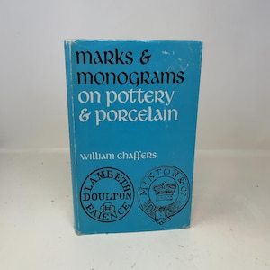 Może przedstawiać: Książka w twardej oprawie zatytułowana "Marks & Monograms on Pottery & Porcelain" autorstwa Williama Chaffersa. Okładka w kolorze jasnoniebieskim z białym tekstem i dwoma okrągłymi logotypami. Przewodnik po ceramice i porcelanie.