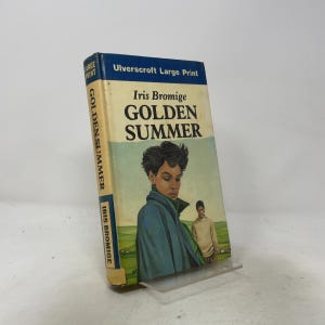 May include: A hardcover book titled Golden Summer by Iris Bromige, published by Ulverscroft Large Print. The cover features an illustration of a person in a blue coat in the foreground and a person in a beige sweater in a green field background.