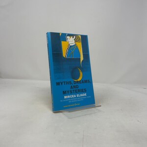 May include: A hardcover book titled "Myths, Dreams, and Mysteries" by Mircea Eliade. The book has a blue cover with a graphic illustration of a person and a crescent moon. The book is propped up on a clear plastic stand.