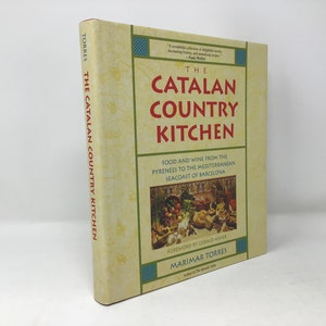 May include: A book titled "The Catalan Country Kitchen: Food and Wine from the Pyrenees to the Mediterranean Seacoast of Barcelona" by MariMar Torres. The cover features a still life of fresh produce and a rustic kitchen setting.