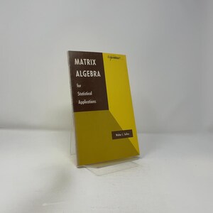 以下が含まれることがあります： 「MATRIX ALGEBRA for Statistical Applications」というタイトルの本で、黄色と茶色の表紙です。透明なプラスチック製のスタンドに立ててあります。著者の名前、Walter L. Sullins が見えます。