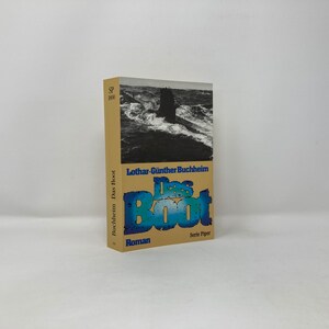May include: A hardcover book titled "Das Boot" by Lothar-Günther Buchheim. The cover shows a black and white image of a submarine at sea. The title is in blue and white, with the word "Roman" below.