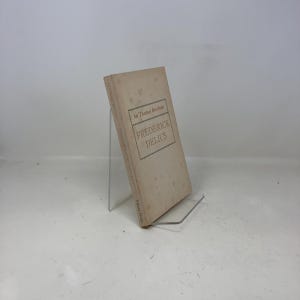 Op de afbeelding: Een vintage boek getiteld "Frederick Delius" door Sir Thomas Beecham. Het boek heeft een lichtbruine kaft met de titel en de naam van de auteur in een donkerbruin lettertype. Het boek wordt gepresenteerd op een transparante acrylstandaard.