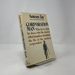 Könnte beinhalten: Ein gebundenes Buch mit dem Titel "CORPORATION MAN" von Antony Jay. Das Cover des Buches ist beige mit schwarzem und braunem Text. Der Untertitel des Buches lautet: "Wer er ist, was er tut, warum seine alten Stammesimpulse das Leben der modernen Corporation beherrschen."