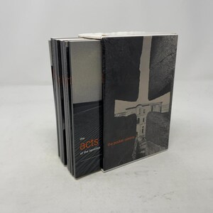 May include: A stack of books with black and white covers. The book on the right has a large cross-shaped design with a building inside. The book on the left has the words "the acts of the apostles" in orange and black.