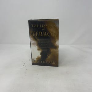 Op de afbeelding: Een hardcover boek getiteld The Lessons of Terror door Caleb Carr. De kaft heeft een donkere, rokerige, bruine en zwarte achtergrond met gouden letters. De ondertitel luidt A History of Warfare Against Civilians: Why It Has Always Failed and Why It Will Fail Again.
