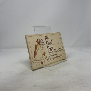 May include: A book titled "No Good Dogs" with a tan cover. The cover features an illustration of a brown and white dog with a stethoscope. The book is propped up on a clear plastic stand.