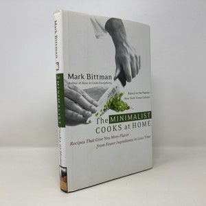 May include: A white hardcover book titled "The Minimalist Cooks at Home" by Mark Bittman. The book cover features a photo of a hand holding a knife and chopping herbs.