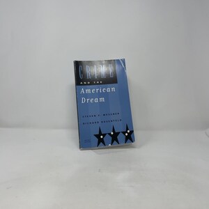 May include: A book titled "Crime and the American Dream" by Steven F. Messner and Richard Rosenfeld. The cover is blue with white text and three black star graphics. The book is slightly angled, with a white background.