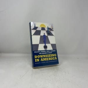 May include: A paperback book titled Downsizing in America: Reality, Causes, and Consequences by William J. Baumol, Alan S. Blinder, and Edward N. Wolff. The cover features a graphic of figures on a black and white checkered board under a yellow sun.