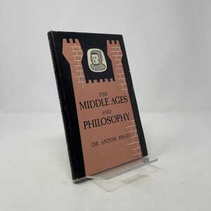 Puede incluir: Un libro de tapa dura titulado "The Middle Ages and Philosophy" del Dr. Anton Pegis. La portada negra presenta una ilustración marrón de un castillo y un retrato. El libro se exhibe en un soporte transparente.