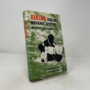 May include: A hardcover book titled Aikido and the Dynamic Sphere: An Illustrated Introduction by A. Westbrook and O. Ratti. The cover features a green and white marbled background with a black ink illustration of figures practicing aikido.