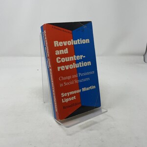 May include: A hardcover book titled "Revolution and Counter-revolution" by Seymour Martin Lipset. The book has a blue and red cover with white text. The book is displayed on a clear plastic stand.
