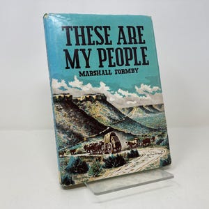 Puede incluir: Un libro de bolsillo vintage titulado "These Are My People" de Marshall Formby. La portada presenta un paisaje escénico con una caravana de carros viajando por un valle.