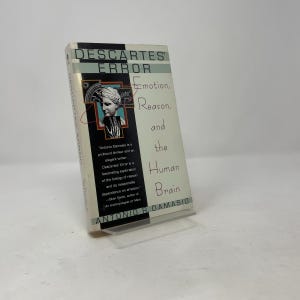 May include: A paperback book titled Descartes' Error: Emotion, Reason, and the Human Brain by Antonio R. Damasio. The cover features a cream background, a black vertical panel, and a small illustration of a classical bust and a hand.