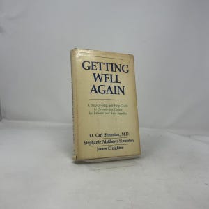 Puede incluir: Un libro titulado "GETTING WELL AGAIN" con una cubierta beige y texto azul. Es una guía de autoayuda para superar el cáncer, escrita por O. Carl Simonton, Stephanie Matthews-Simonton y James Creighton.