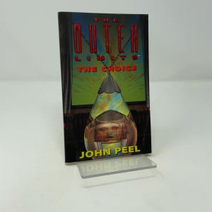May include: A paperback book titled The Outer Limits: The Choice by John Peel. The cover features a large, metallic, cone-shaped pendant hanging from a chain against a green and yellow background, with a dark, shadowy interior scene visible below.