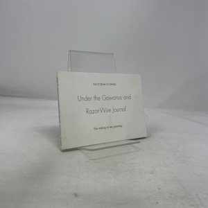 以下が含まれることがあります： ラックストロー・ダウネス著の「Under the Gowanus and Razor-Wire Journal」というタイトルの白い本。透明なアクリルスタンドに展示されています。「The making of two paintings」というテキストも表示されています。本のタイトルは黒色です。