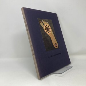 May include: A navy blue book titled "Journey to the Self-Portrait" by Bernard Maisner. The cover features a painting of a foot with a circular design on the sole.