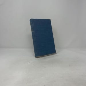 May include: A hardcover book with a blue cover. The book is standing upright on a white surface. The spine of the book is visible, with text printed vertically. The book's pages are slightly yellowed.