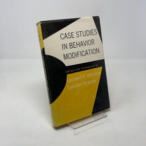 以下が含まれることがあります： 「Case Studies in Behavior Modification」というタイトルのヴィンテージ本。黒、白、黄色の表紙。透明なプラスチック製のスタンドに立てかけられています。テキストには、Leonard P. UllmannとLeonard Krasnerの名前が含まれています。