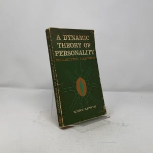 May include: A green book titled "A Dynamic Theory of Personality: Selected Papers" by Kurt Lewin. The cover features a stylized illustration of a person with arrows pointing towards them.