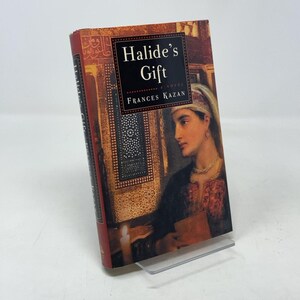 May include: A hardcover book titled "Halide's Gift" by Frances Kazan. The cover features a portrait of a woman in a headscarf and jewelry, set against a backdrop of ornate architectural details. The book has a red spine.