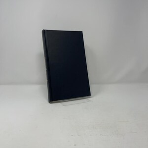 May include: A hardcover book with a solid dark navy blue cover. The spine of the book features gold-colored text that is partially visible, indicating the title. The book is positioned upright, showcasing its rectangular shape and clean, smooth surface.