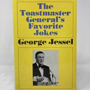 Op de afbeelding: Een geel boek met de titel "The Toastmaster General's Favorite Jokes" van George Jessel. De omslag heeft blauwe tekst en een zwart-witfoto van een man in smoking die op een podium spreekt.