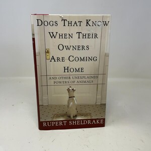 Pode incluir: Um livro de capa dura intitulado "Dogs That Know When Their Owners Are Coming Home" de Rupert Sheldrake. A capa do livro apresenta uma ilustração de um cão em frente a uma porta. A lombada do livro é vermelha.