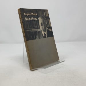 Può includere: Un libro intitolato "Eugenio Montale Selected Poems" con una foto dell'autore in copertina. Il libro è marrone con una costa gialla.