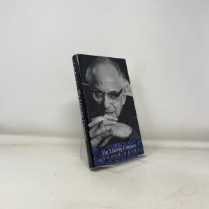 Könnte beinhalten: Ein Hardcover-Buch mit dem Titel "The Listening Composer" von George Perle. Das Cover zeigt ein Schwarz-Weiß-Porträt eines Mannes mit Brille. Das Buch wird auf einem transparenten Acrylständer präsentiert.