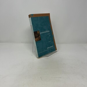 Può includere: Un libro intitolato "potentialities" di Giorgio Agamben, esposto su un supporto in acrilico trasparente. Il libro ha una copertina turchese con scritte dorate e un dorso marrone. La copertina presenta un ritratto ed elementi decorativi.