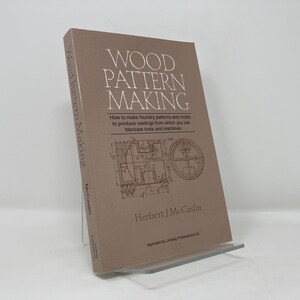Op de afbeelding: Een bruin boek getiteld "Wood Pattern Making" door Herbert J. McCaslin. De omslag van het boek toont een diagram van een gietmodel.