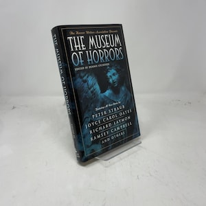 Puede incluir: Un libro de tapa dura titulado "THE MUSEUM OF HORRORS" de The Horror Writers Association. La portada presenta una imagen azul oscuro de una estatua y los nombres de varios autores, incluidos Peter Straub y Joyce Carol Oates.