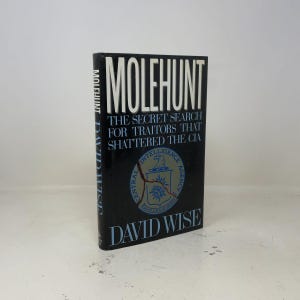 May include: A hardcover book titled Molehunt: The Secret Search for Traitors That Shattered the CIA by David Wise. The black cover features white text and a Central Intelligence Agency emblem that appears to be cracked by a jagged red line.