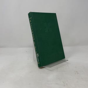 May include: A green hardcover book titled Faulkner The Major Years with gold lettering on the spine. The front cover features a subtle embossed leaf design. The book is displayed upright on a clear stand, showing the title and author clearly.