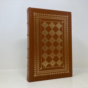 Peut inclure: Un livre relié en cuir marron avec un motif doré sur la couverture. Le motif présente un motif répétitif de fleurs stylisées.
