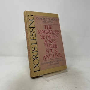 May include: A hardcover book titled Canopus in Argos: Archives, The Marriages Between Zones Three, Four, and Five by Doris Lessing. The cover is tan with a large pink rectangular center panel containing dark red text and black lettering.