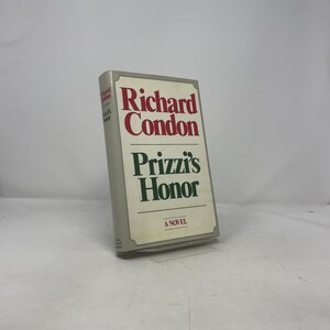 Puede incluir: Un libro de tapa dura titulado "Prizzi's Honor" de Richard Condon. El libro tiene una cubierta gris claro con texto rojo y verde. El título y el nombre del autor se muestran en la portada.