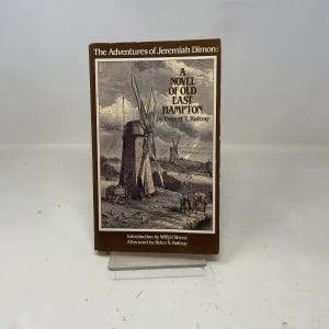 May include: A hardcover book titled "The Adventures of Jeremiah Dimon: A Novel of Old East Hampton" by Everett T. Rattray. The cover features a sepia-toned illustration of windmills and figures, with text in a serif font. The book is brown.