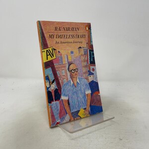May include: A paperback book titled My Dateless Diary: An American Journey by R.K. Narayan. The cover features a colorful, textured illustration of a person with glasses in a city setting, with a yellow 5th Ave street sign and urban buildings.