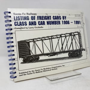 May include: A spiral bound book titled "Santa Fe Railway Listing of Freight Cars by Class and Car Number 1906-1991" with a black and white illustration of a freight car on the cover. The book was compiled by Larry Occhiello and published by the Santa Fe Modelers Organisation, Inc. and the Santa Fe Railway Historical Society.