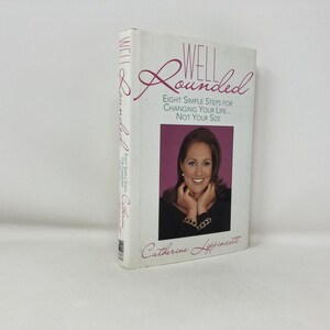 Può includere: Un libro con copertina rigida intitolato "Well Rounded" con un ritratto di donna sulla copertina. Il titolo del libro è in corsivo e il sottotitolo recita "Eight Simple Steps for Changing Your Life... Not Your Size."