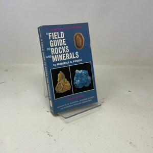 May include: A blue book titled "A Field Guide to Rocks and Minerals" by Frederick H. Pough. The book features images of rocks and minerals, with text on the spine. The book is a fourth edition, sponsored by the National Audubon Society and National Wildlife Federation.