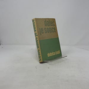 Pode incluir: Um livro intitulado "dalec je sonce" de Dobrica Ćosić. A capa é bege e verde, com o título e o nome do autor em verde. O livro é exibido em um suporte de acrílico transparente.