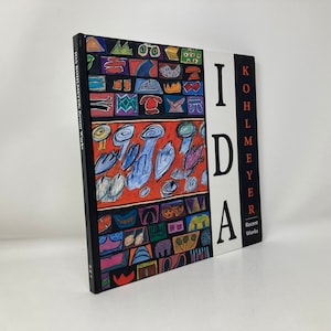 May include: A book titled "Ida Kohlmeyer: Recent Works" with a colorful abstract painting on the cover. The cover features a variety of shapes and colors, including red, blue, yellow, and green.