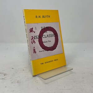 May include: A paperback book titled Zen and Zen Classics Volume One by R.H. Blyth, published by The Hokuseido Press. The cover features a bright yellow border, a central white panel with a maroon circle, black text, and red Japanese calligraphy.